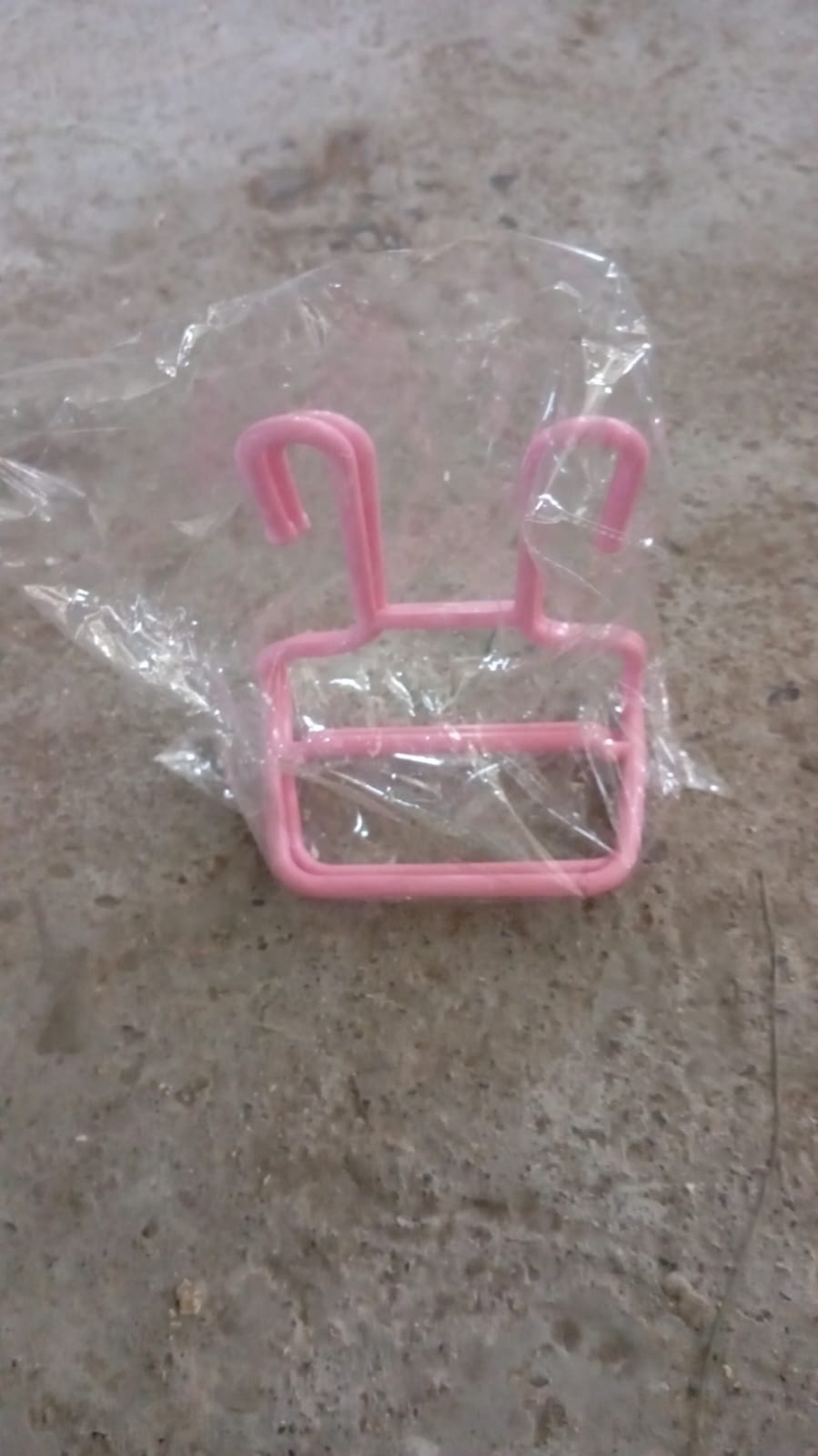 A single pink plastic shoe drying rack is sealed inside a clear plastic bag on a textured grey surface.