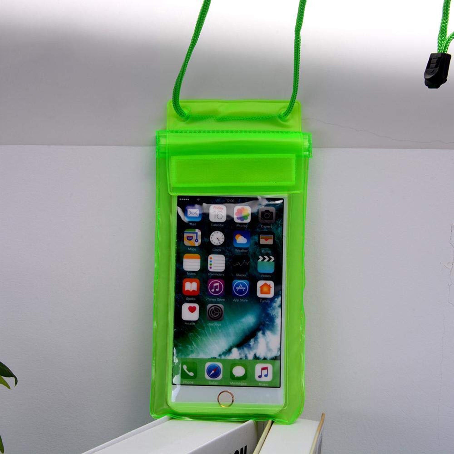 A green waterproof phone pouch holds a smartphone displaying app icons, hanging against a light-colored wall.