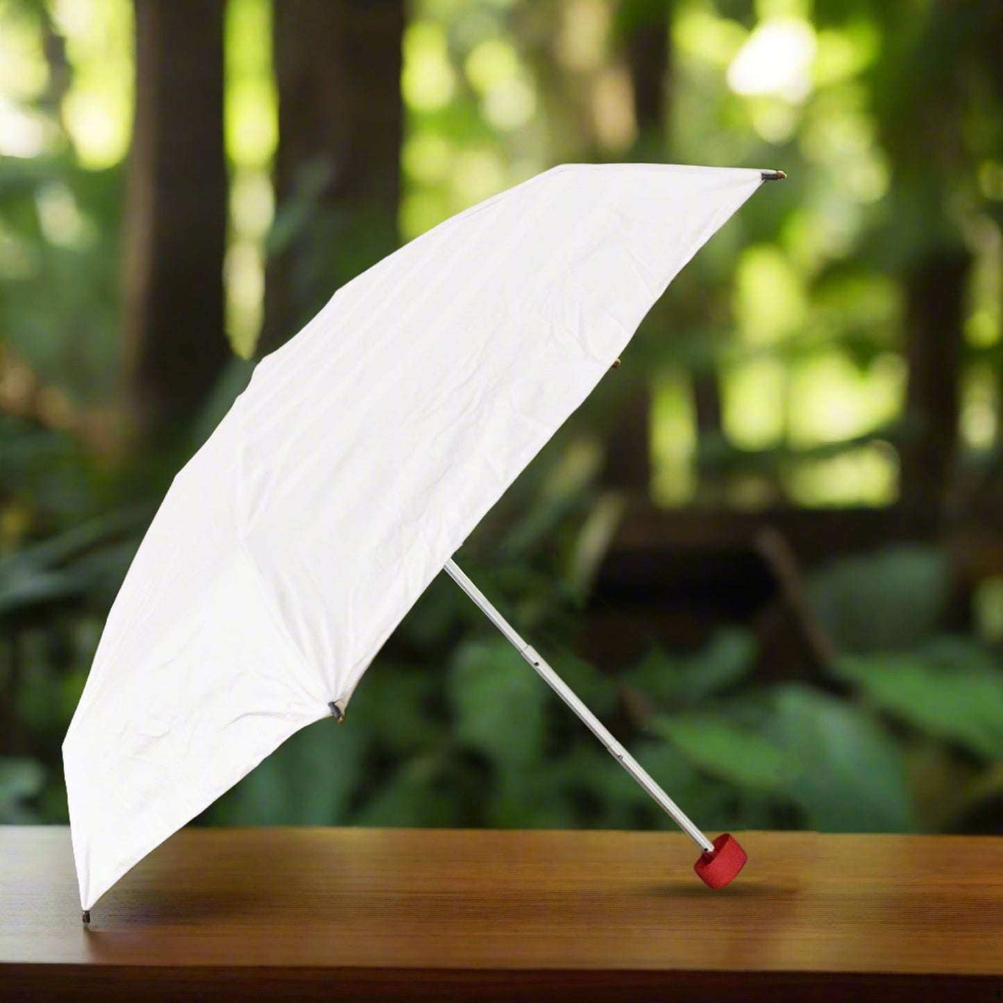 An open white umbrella with a red handle sits on a wooden surface, with green foliage in the background.