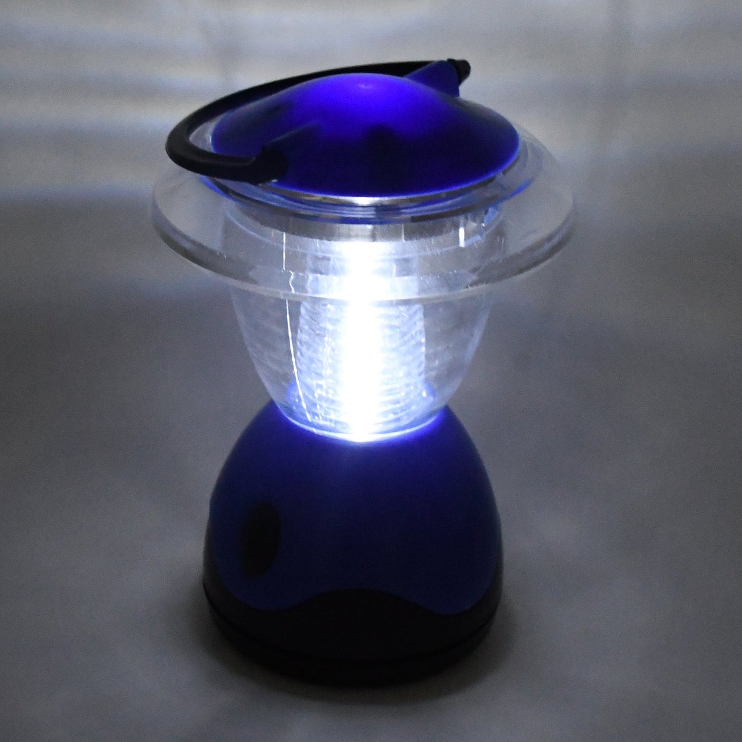 The blue and clear plastic lantern is brightly illuminated, casting a glow on the surrounding gray surface.