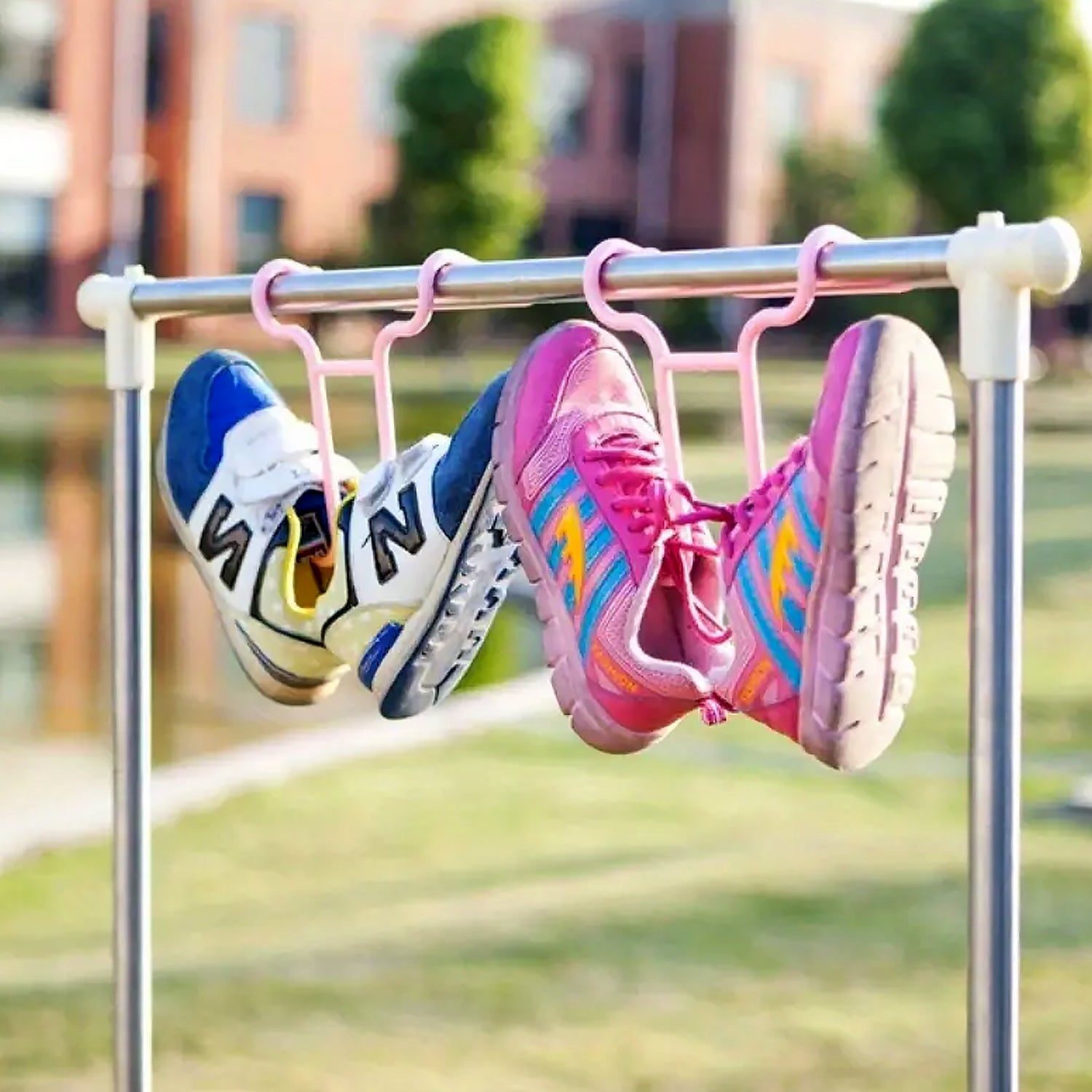 Two pairs of colorful athletic shoes hang from pink plastic drying racks on a metal clothesline outdoors.