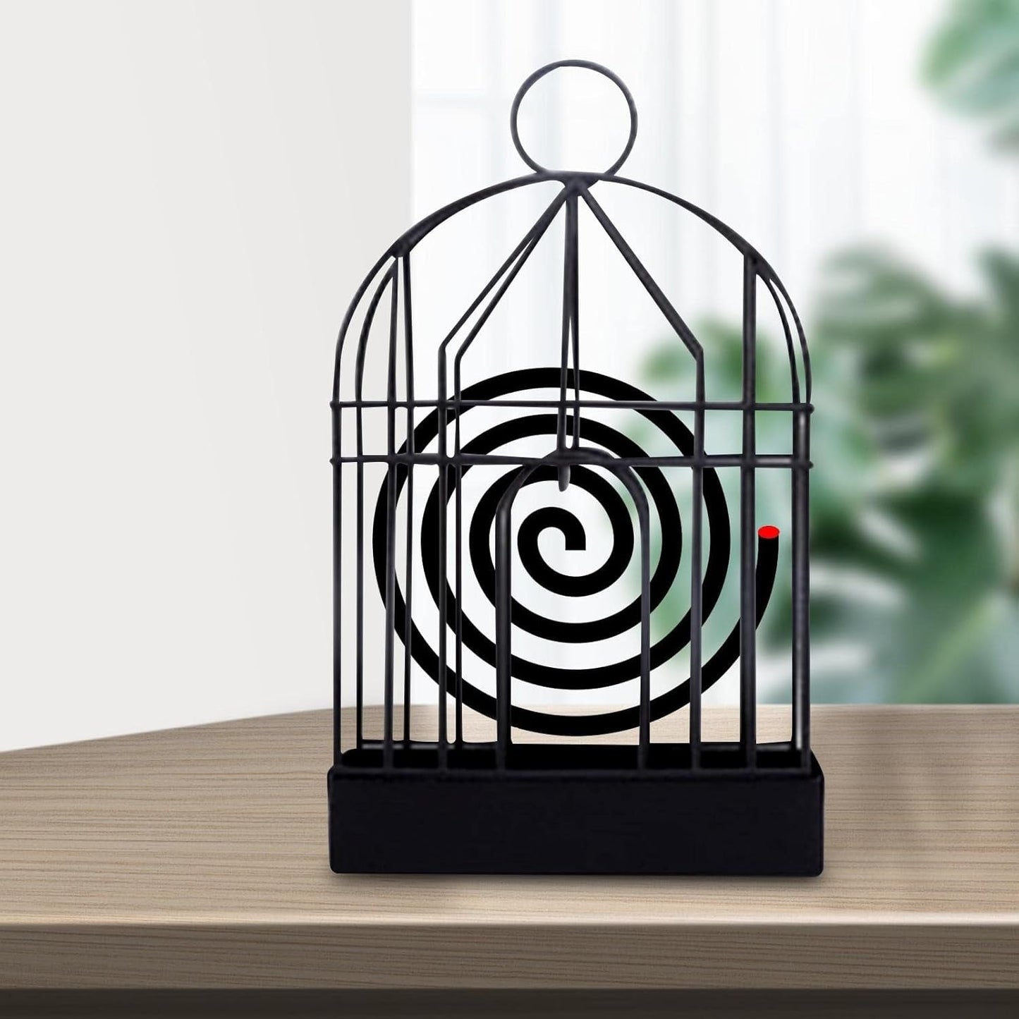 A black iron birdcage-style holder with a burning mosquito coil inside sits on a light wooden table.