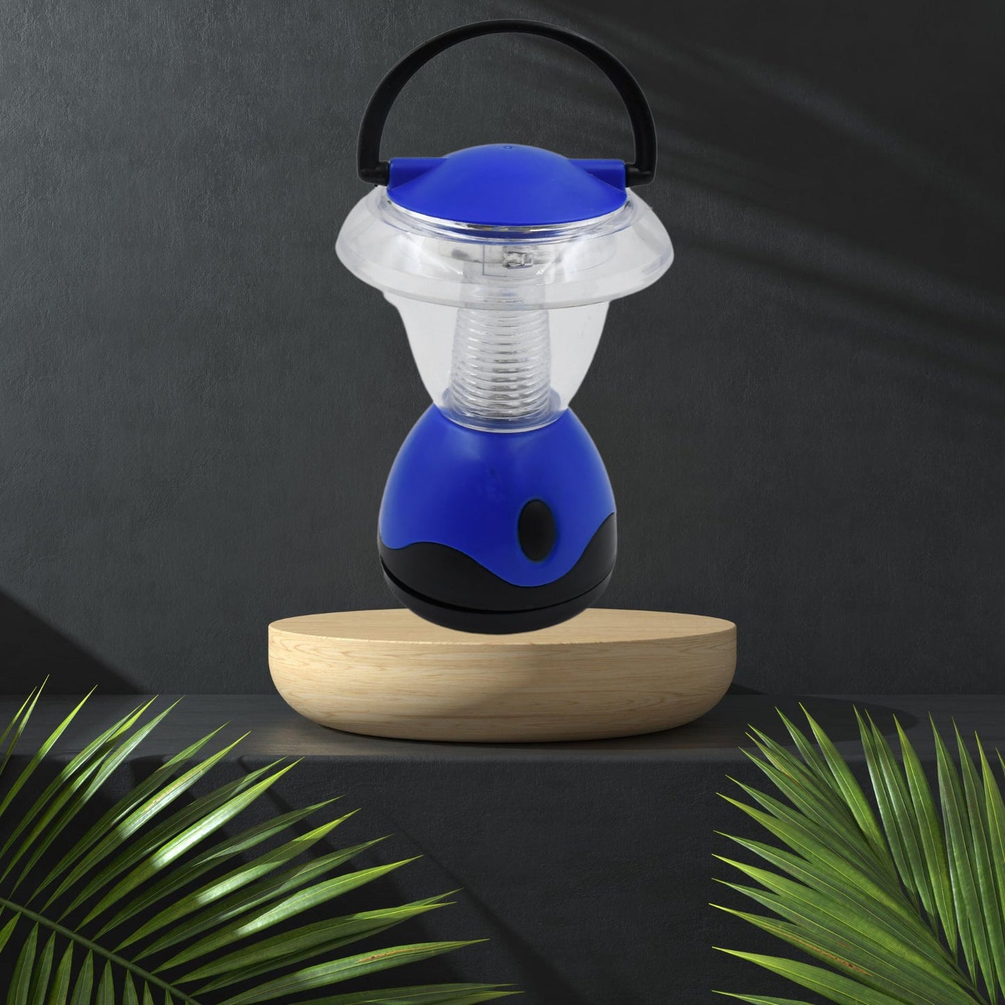 The blue and clear plastic mini lantern rests on a light wooden pedestal, flanked by green palm fronds against a dark