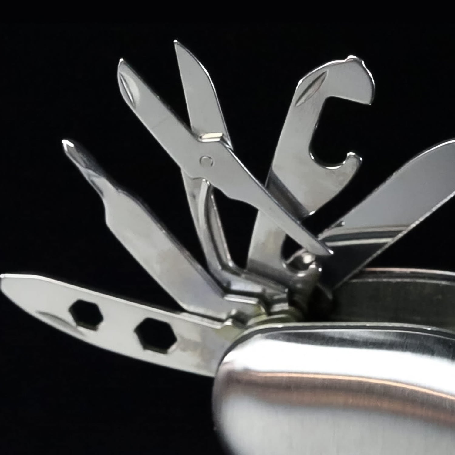 A close-up of the silver multi-tool's various metal tools extended, including scissors, a bottle opener, and a hex wrench.