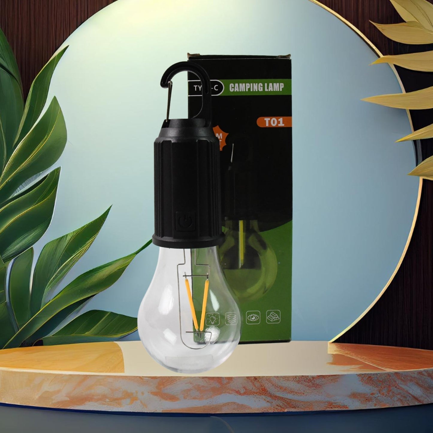 A black and clear portable LED tent light with a black carabiner hangs in front of its green and black packaging, set
