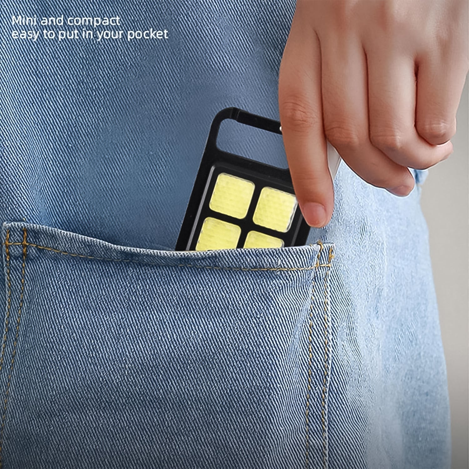 A hand slides the compact black LED keychain light with four yellow squares into the back pocket of blue jeans.