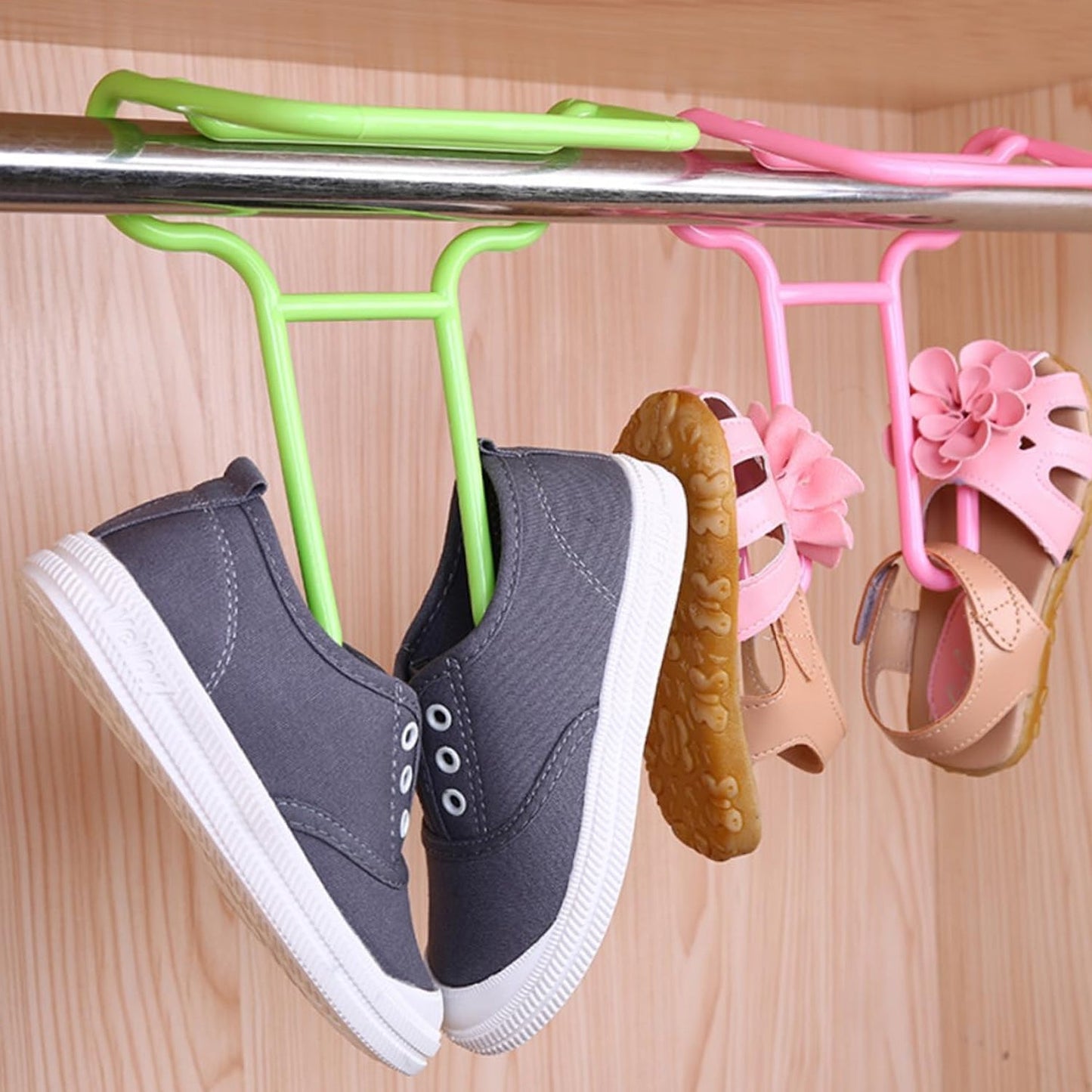 A pair of grey canvas shoes and pink sandals hang from green and pink plastic Organivo shoe drying racks on a metal rod.