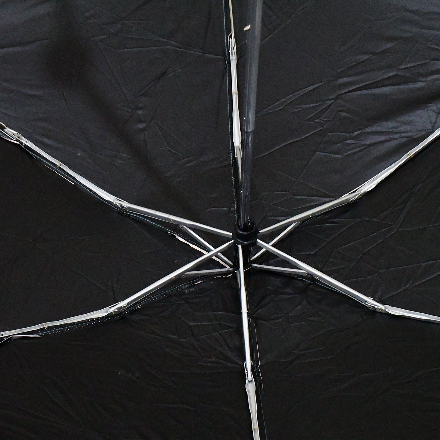 The interior of a black umbrella reveals its silver metal spokes and central mechanism.