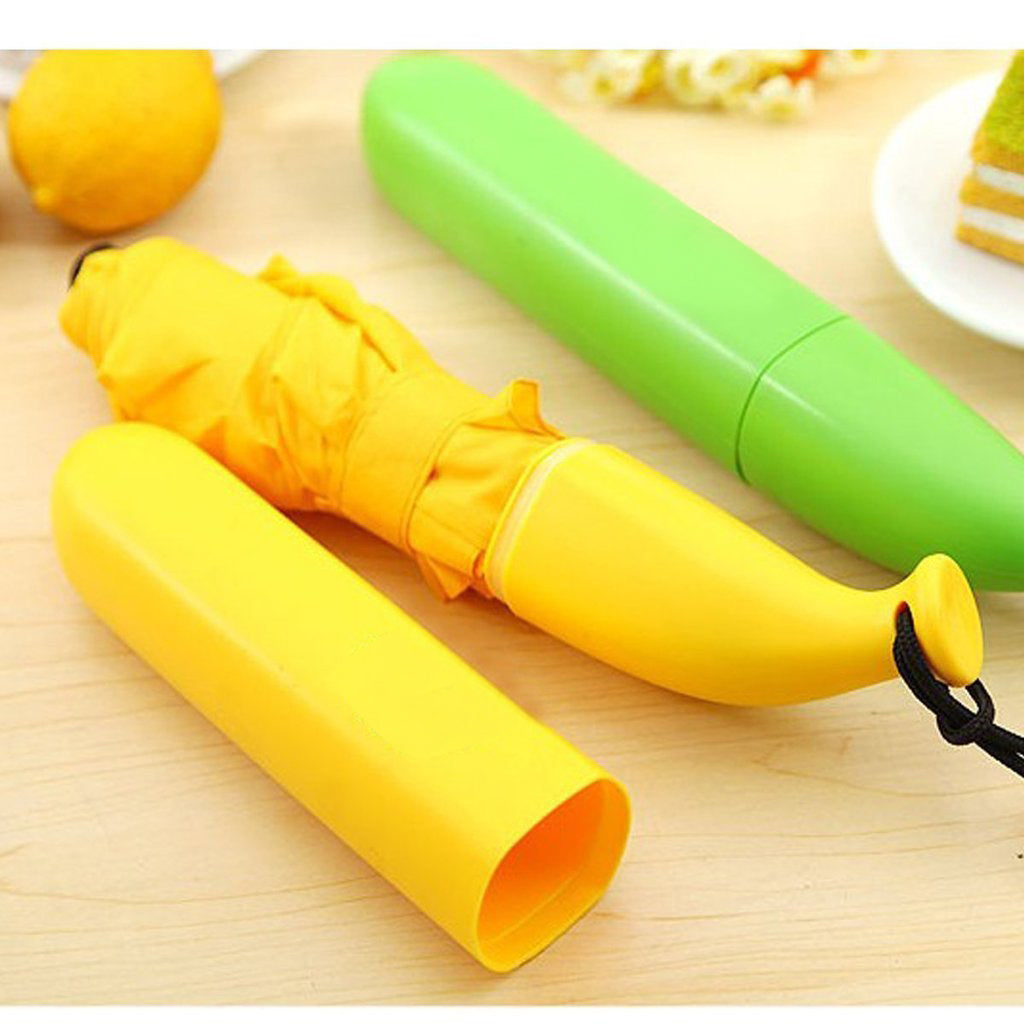 A yellow banana-shaped umbrella, partially out of its case, lies on a wooden surface next to a green banana case.