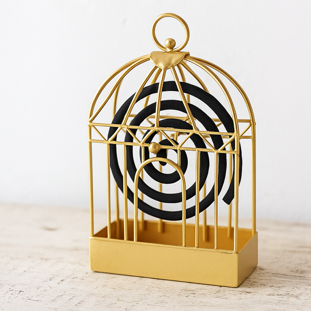 A shiny gold metal birdcage-style holder contains a black mosquito coil on a light wooden surface.