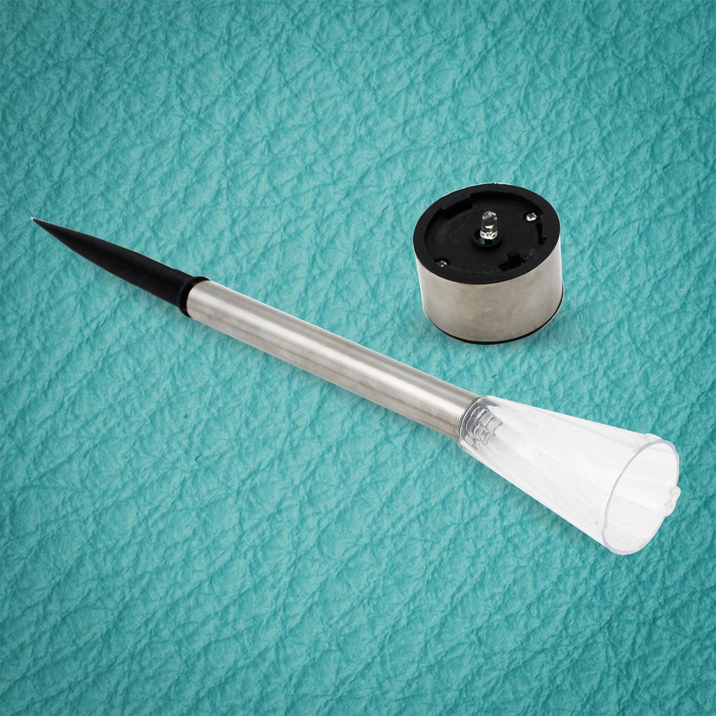 A disassembled solar LED light shows the silver stake with black spike and the separate silver and black solar cap.
