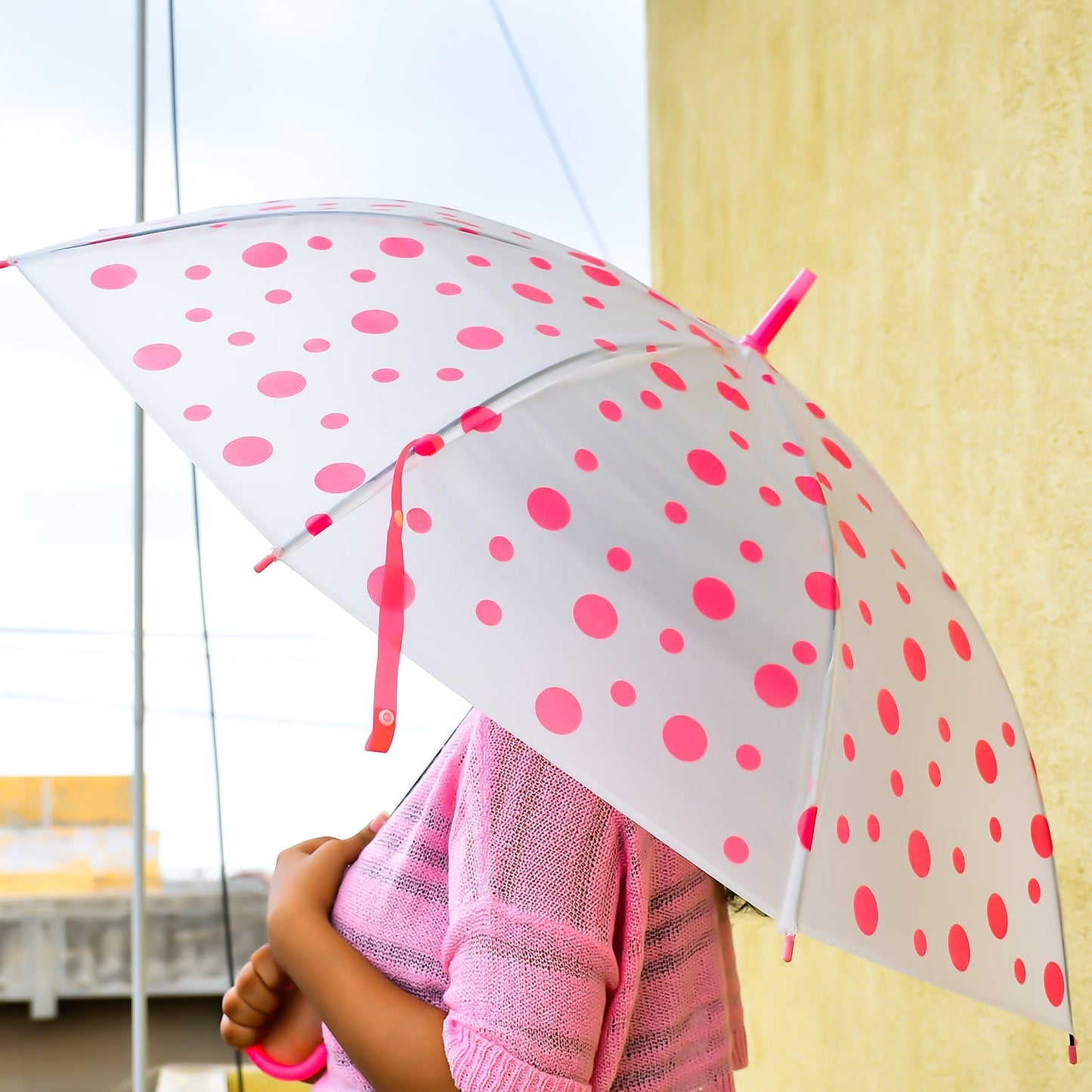 A person holds a white umbrella with bright pink polka dots, featuring a matching pink handle and tip.