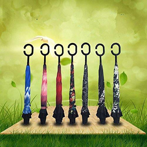 Seven closed reverse umbrellas with C-shaped handles stand upright on a wooden board against a green, leafy background.