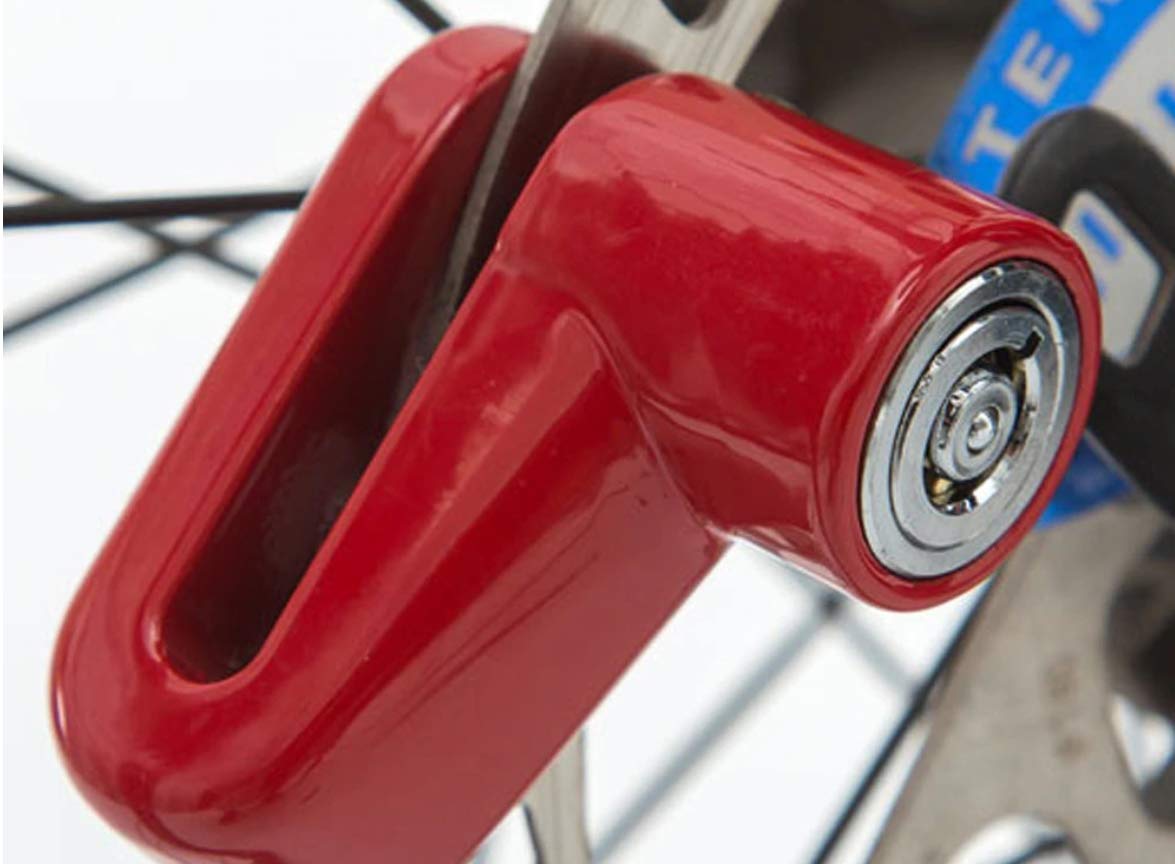 A close-up of a red motorcycle wheel security device clamped onto a bicycle disc brake, showing the silver lock mechanism.