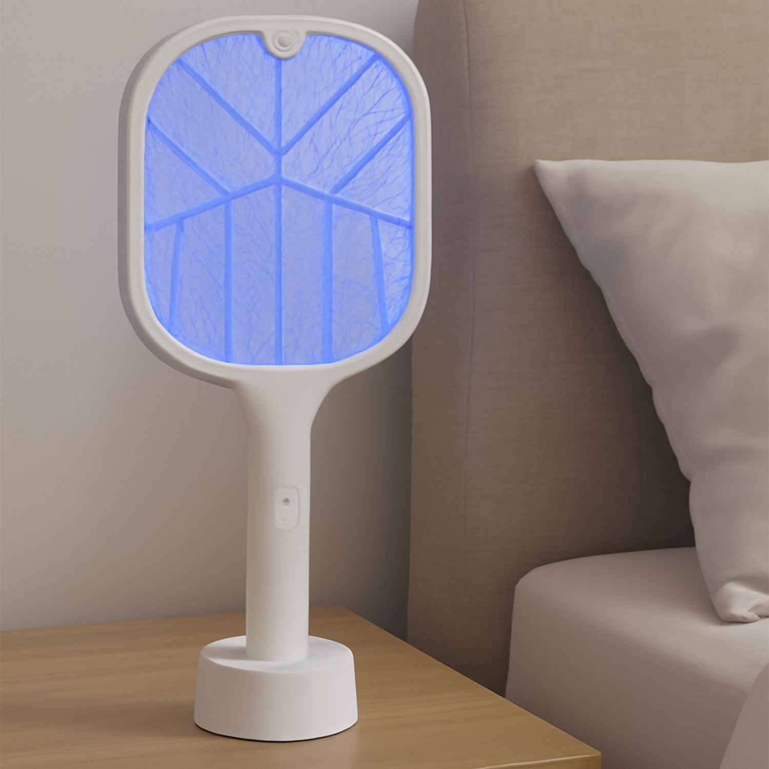 A white FlyTamer mosquito killer racket with a glowing blue UV light stands on a wooden nightstand next to a bed.