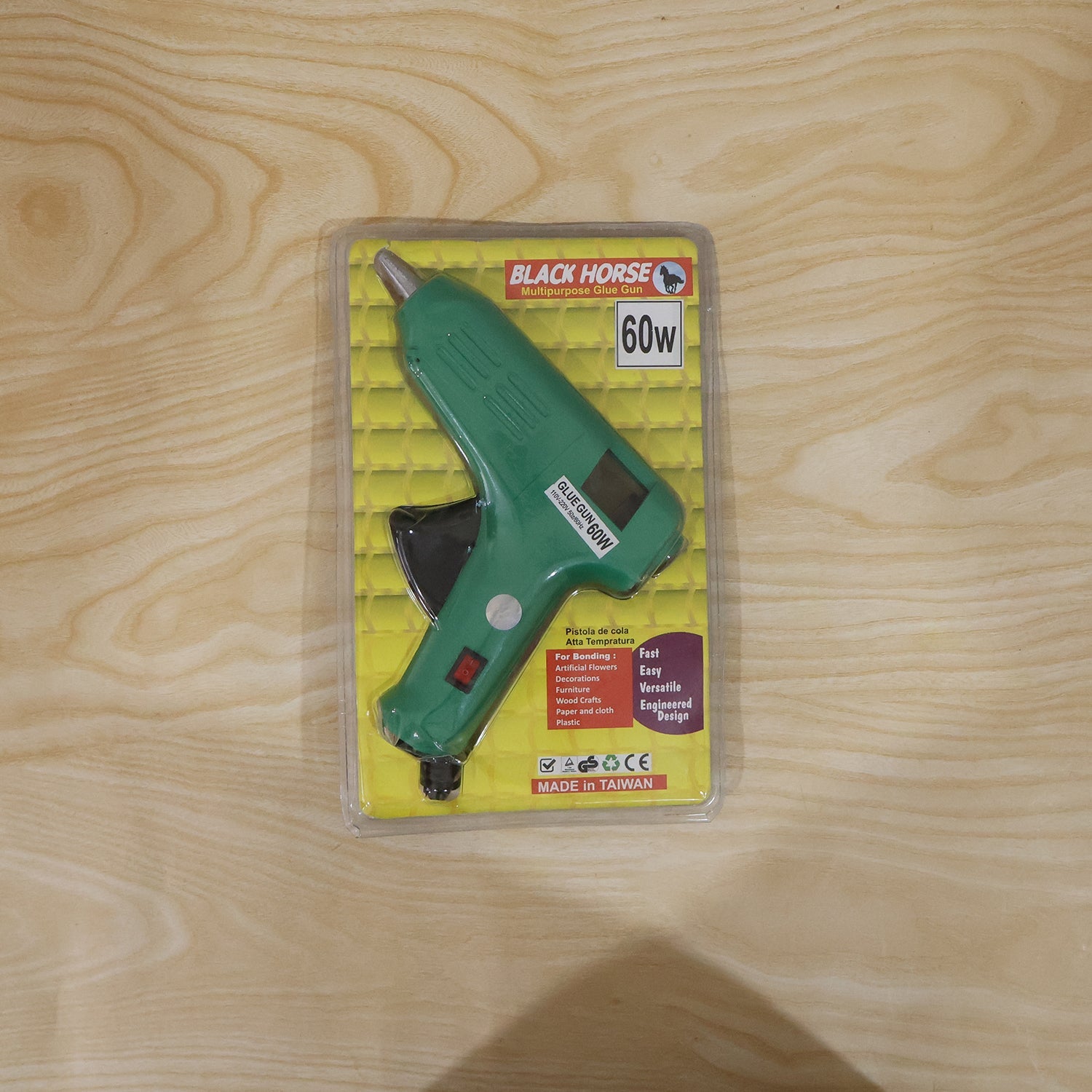 A green 60 Watt hot melt glue gun on a workbench, surrounded by crafting materials and tools.