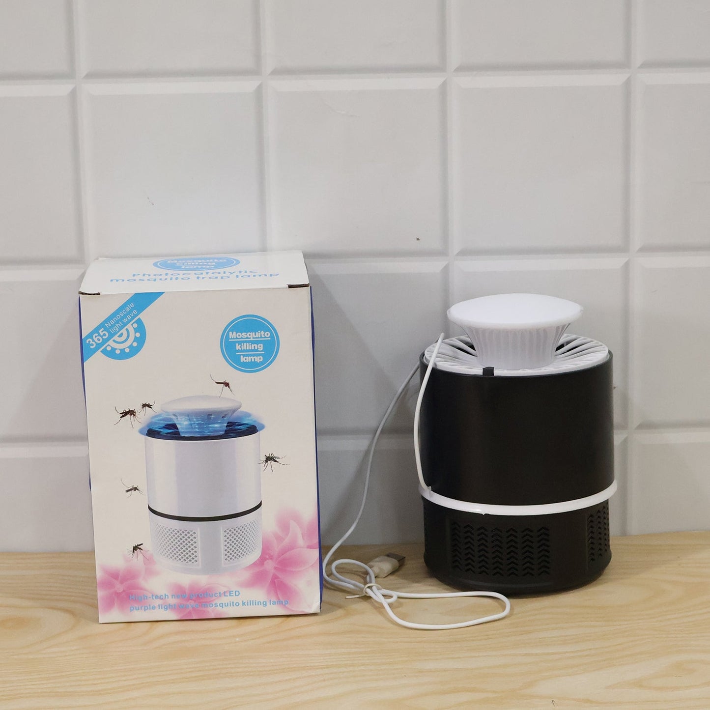 A black and white Mosquito Killer Lamp next to its product box, both on a wooden surface against a white tiled wall.