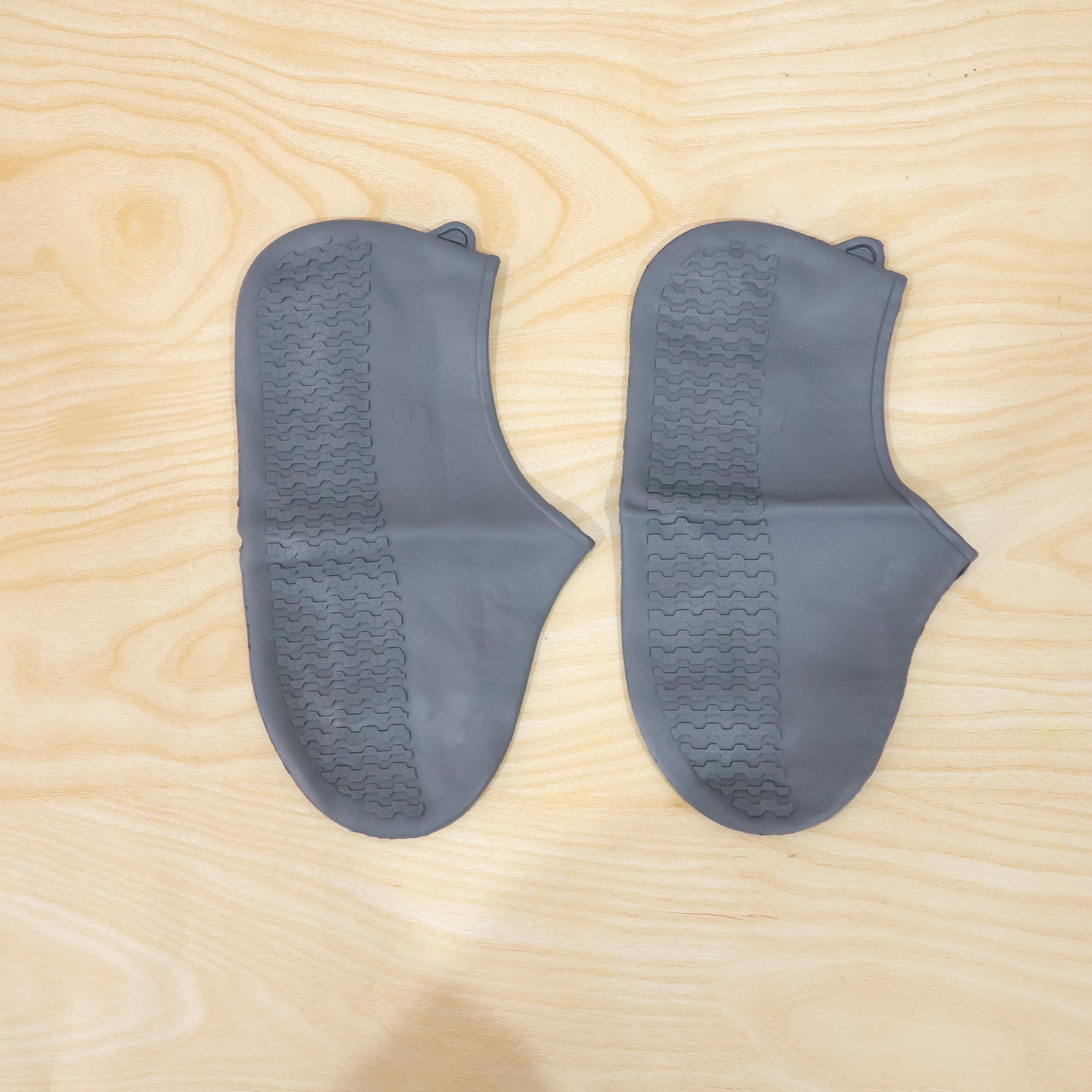 Two gray silicone foot protectors with textured soles are neatly arranged on a light wooden surface.