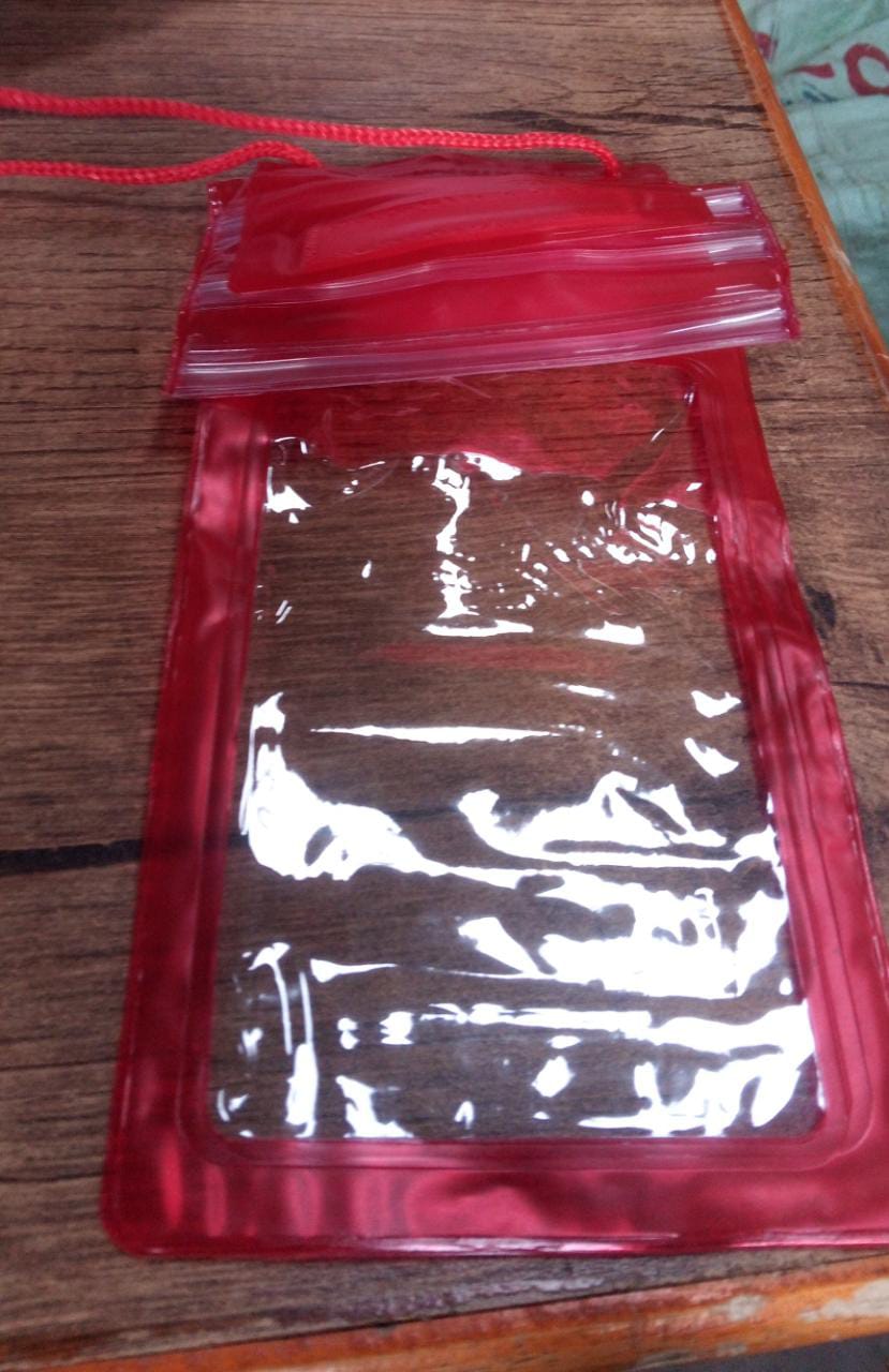 A red waterproof mobile pouch with a clear front and a matching lanyard is shown lying flat on a wooden surface.