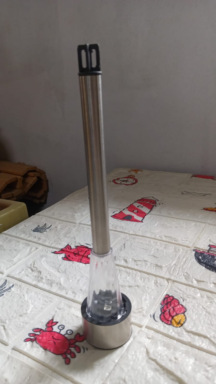 The solar LED spike light stands upright on a white patterned surface with red crabs and lighthouses.
