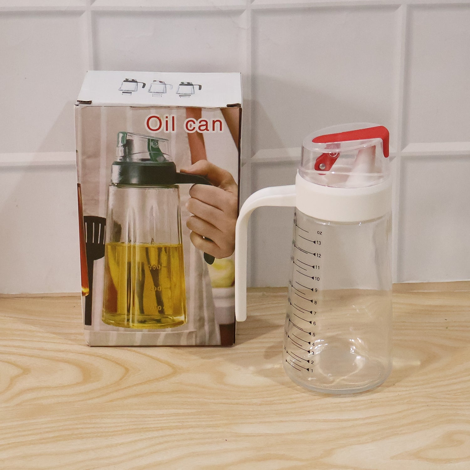 Glass 500ml oil dispenser with white handle and red flip cap beside packaging on wooden surface